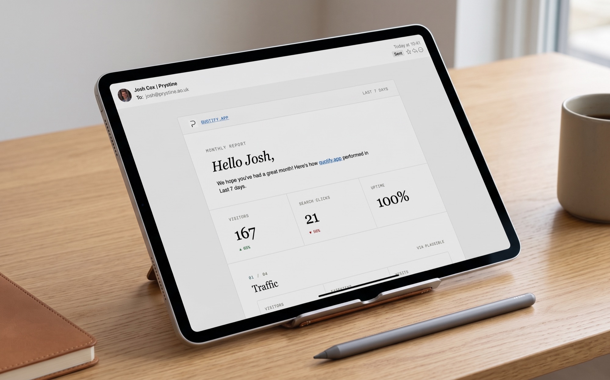 A SendTidings monthly report email open on an iPad on a desk: a branded letter greeting the client by name, with headline figures for visitors, search clicks and uptime.
