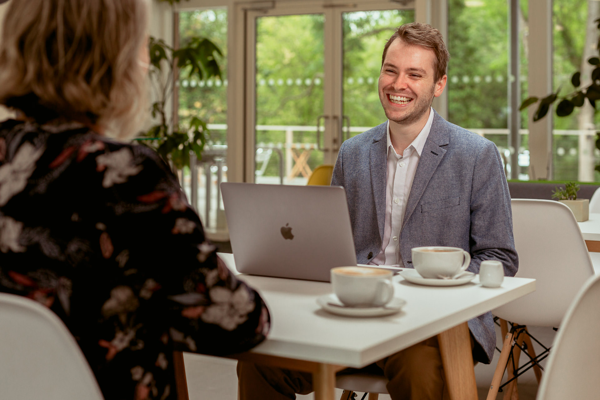 Josh Cox laughing with a client over coffee, laptop open on the table between them